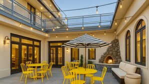 A courtyard with yellow chairs and tables, a stone fireplace, and a balcony with string lights. - The Live Hotel (Los Angeles)