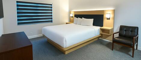 Habitación de hotel con cama, escritorio, silla, mesita de noche y televisor montado en la pared.