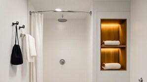 A modern bathroom with a shower, a towel rack, a shelf with towels, and a black bag. - The Live Hotel (Los Angeles)