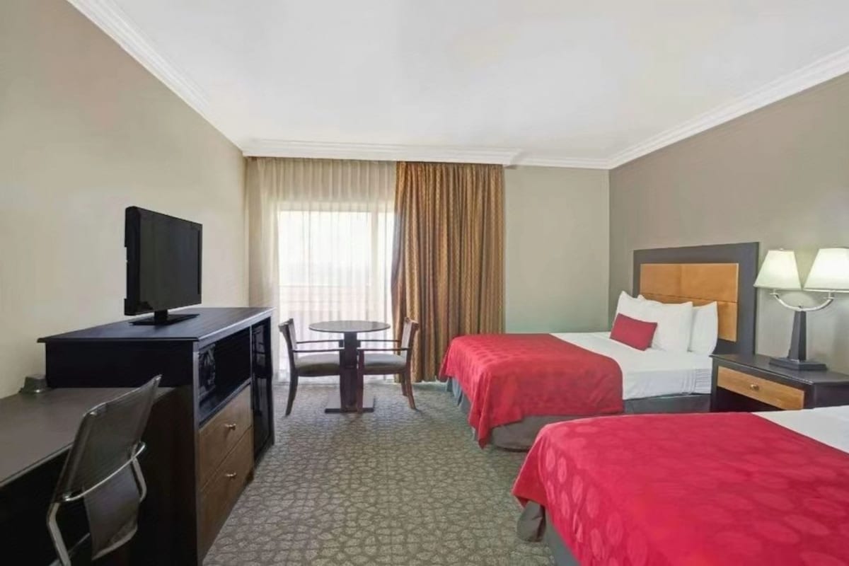Habitación de hotel con dos camas, un escritorio, una silla, un televisor y una ventana con cortinas.