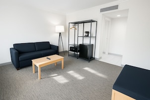 A modern living room with a dark blue sofa, a wooden coffee table, and a black shelving unit with a hanging garment.