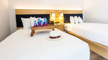 Habitación de hotel con dos camas, cabecero de madera, mesitas de noche y una bandeja con botellas de agua.