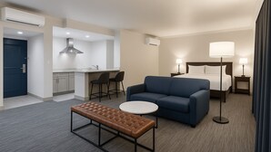 A hotel room with a kitchenette, a sofa, a bed, a bedside table, and a bench. - The Live Hotel (Los Angeles)