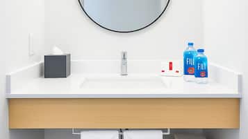 Une salle de bain moderne avec un lavabo blanc, un miroir rond et deux bouteilles bleues posées sur le comptoir.