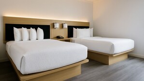 A hotel room with two beds, each with white bedding and a wooden headboard. There are wall-mounted light fixtures above the beds and a bedside table with a phone. - The Live Hotel (Los Angeles)