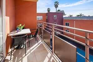A balcony with a table and chairs, a potted plant, and a view of neighboring buildings. - The Live Hotel (Los Angeles)