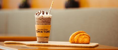 Una taza de postre con la etiqueta 'Specialty Coffee TOM N TOMS' y un croissant sobre una mesa de madera en un café.