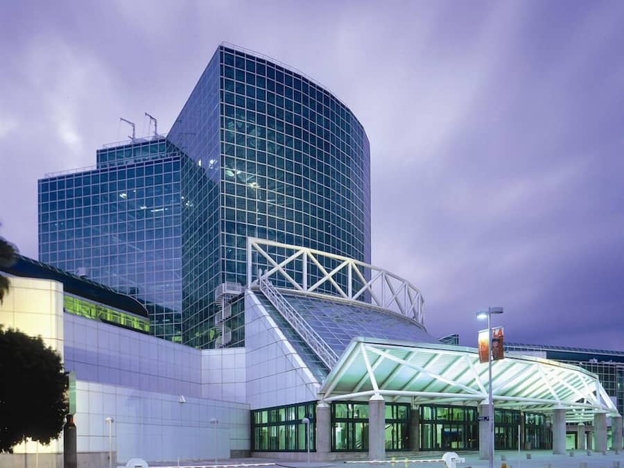 A modern glass building with a unique angular design, featuring a covered entrance area with a glass roof.