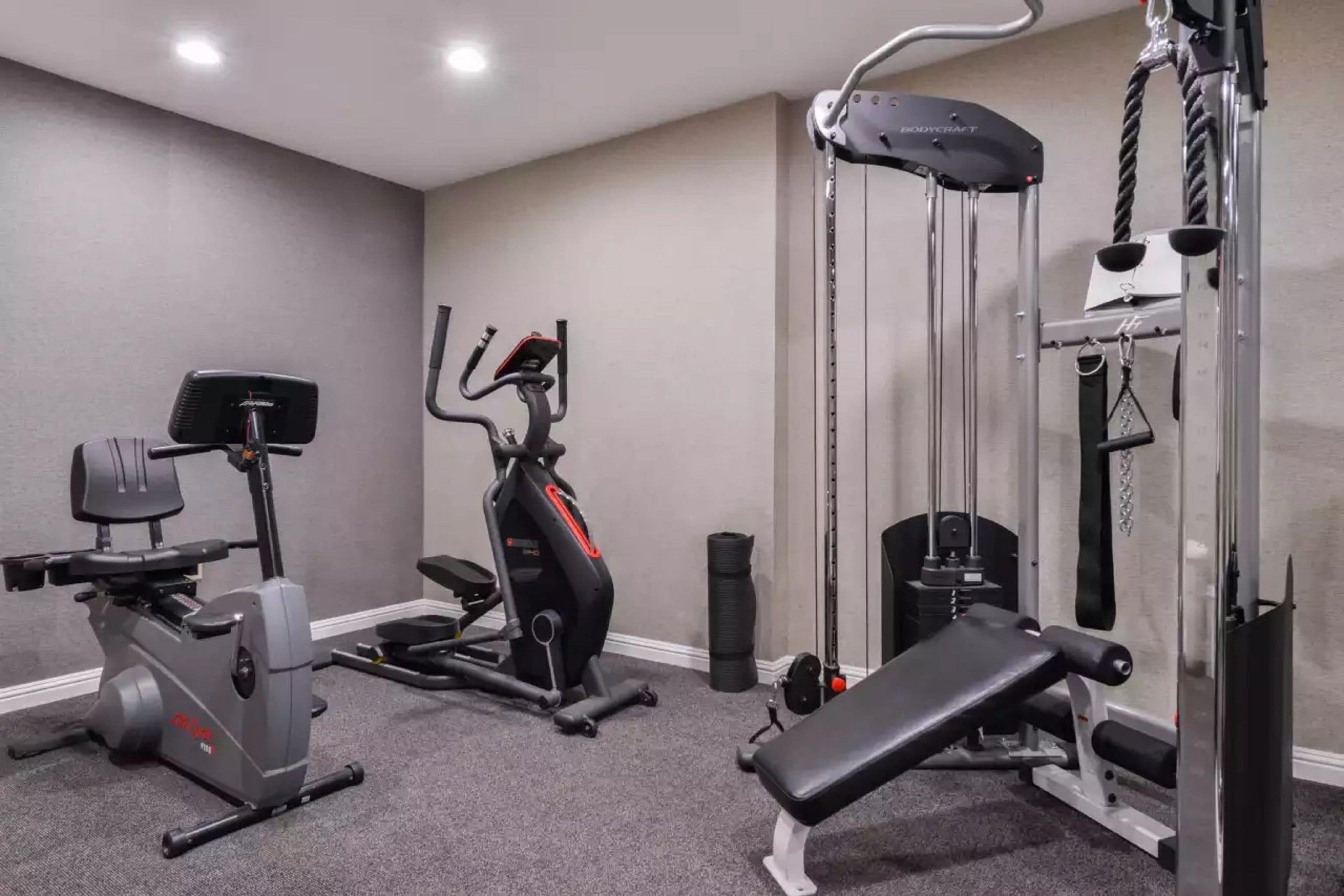 Uma academia com equipamentos de cardio, aparelho de supino e máquina de polia.