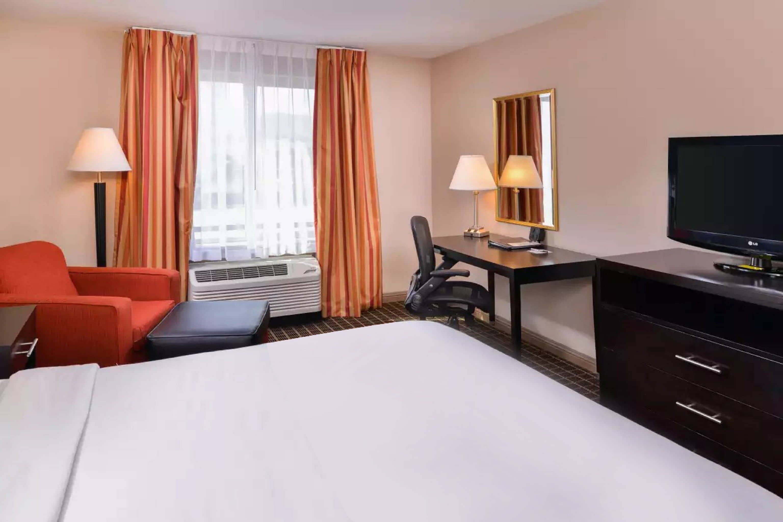 Une chambre d’hôtel équipée d’un lit, d’un bureau, d’une chaise, d’une télévision et d’une fenêtre avec des rideaux.