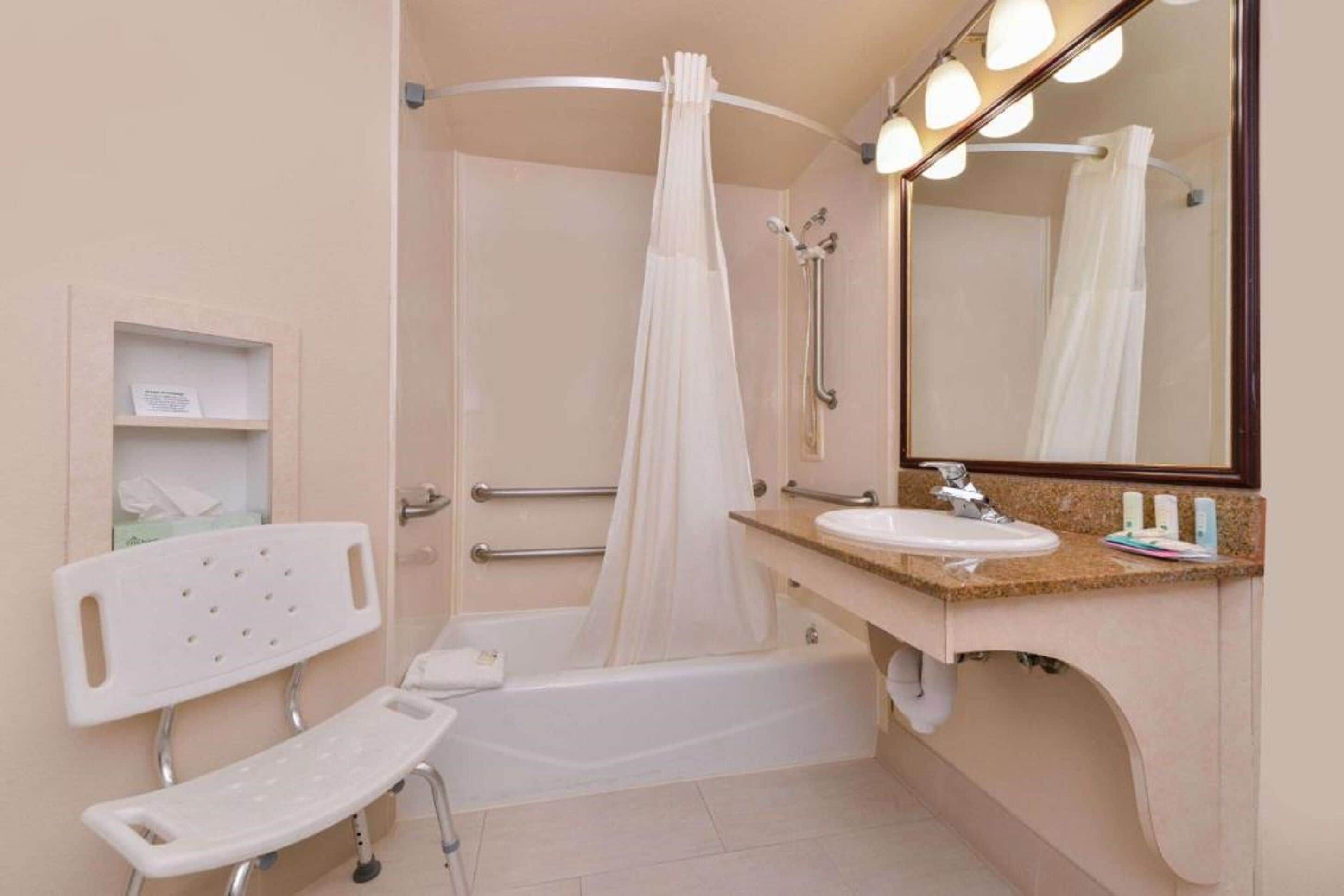 Un baño con bañera, ducha, tocador con lavamanos, espejo y banco.