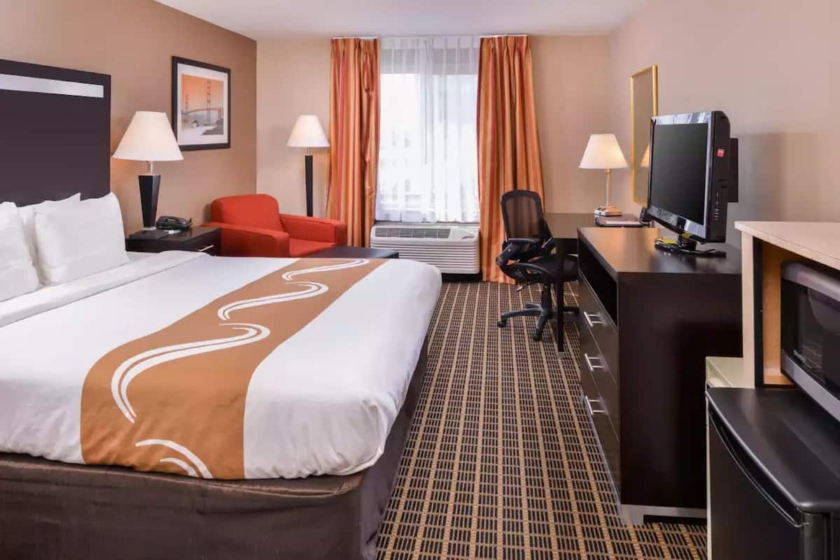 Una habitación de hotel con una cama grande, un escritorio con computadora, un televisor y una silla.