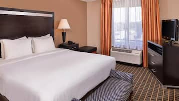 A hotel room with a large bed, a desk with a lamp, a television, and a window with curtains.