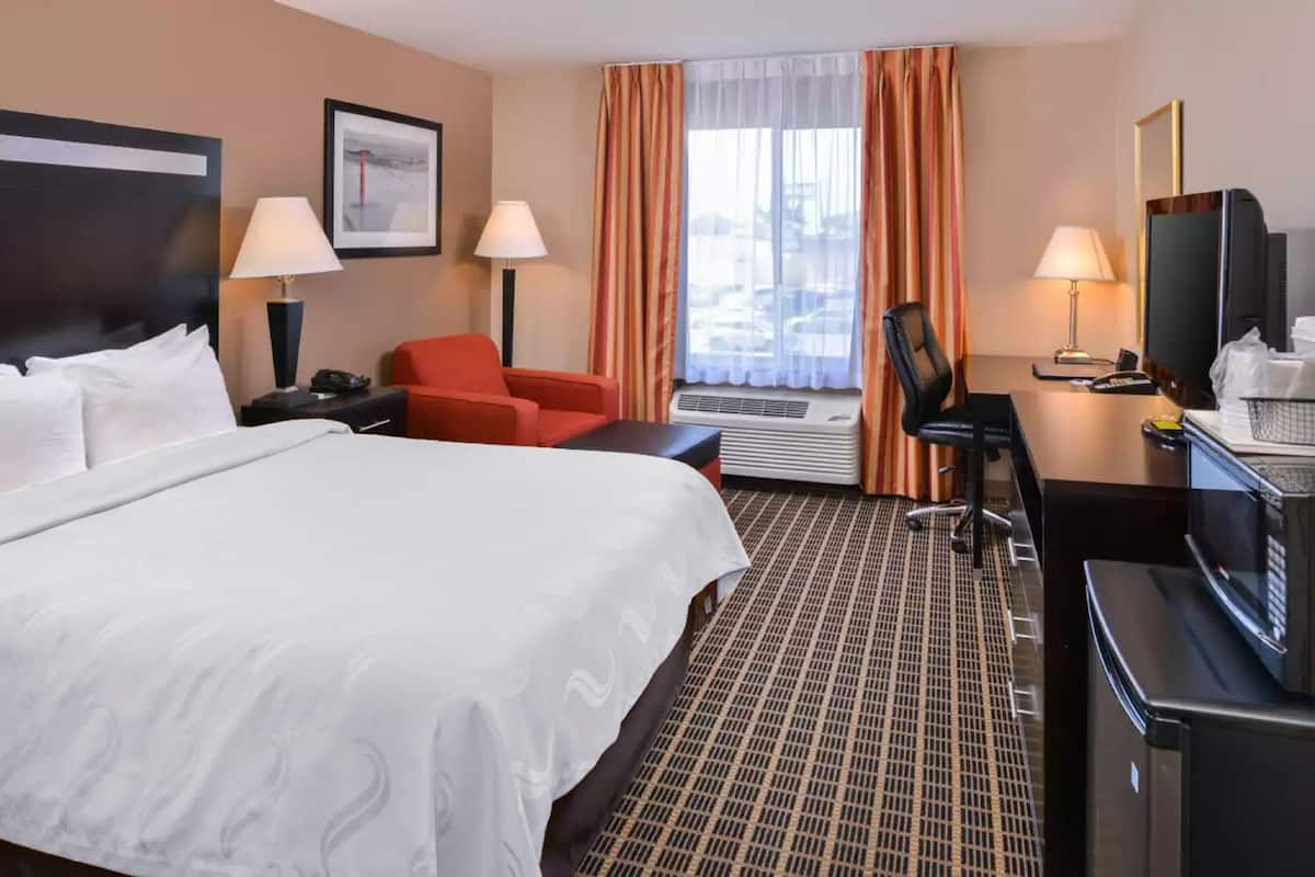Una habitación de hotel con una cama grande, un escritorio con computadora, una silla y un televisor.