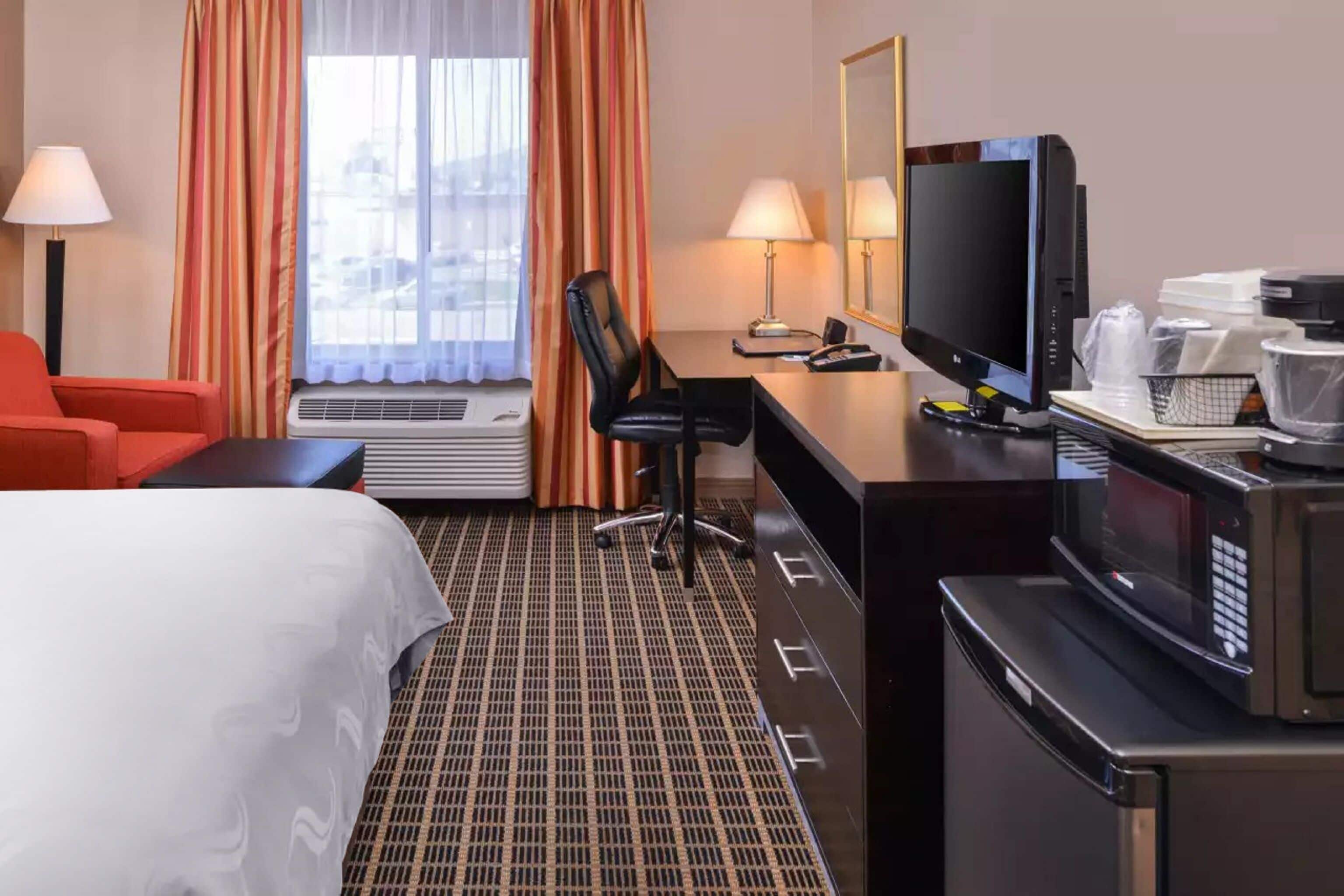 Et hotelværelse med en seng, et skrivebord med en computer, et fjernsyn, en mikroovn og en rød stol.