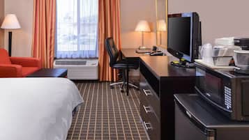 Habitación de hotel con cama, escritorio con computadora, televisión, microondas y una silla roja.