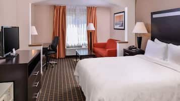 Quarto de hotel com cama, escrivaninha, cadeira, televisão e janela com cortinas.