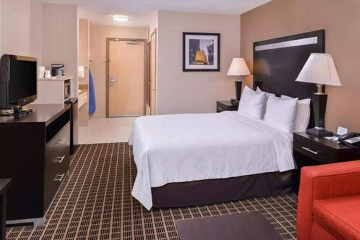 Una habitación de hotel con una cama, un escritorio con computadora, un televisor y una silla roja.