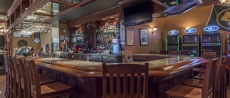 Una zona de bar con sillas de madera, una barra y una variedad de botellas y vasos.