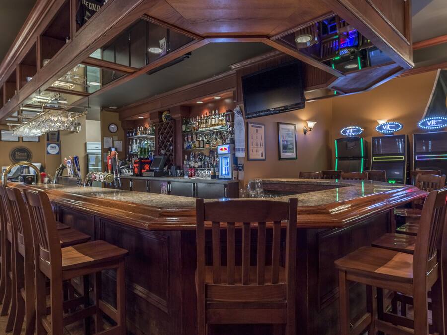 Una zona de bar con sillas de madera, una barra y una variedad de botellas y vasos.