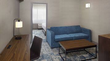 Habitación de hotel con un escritorio de madera, un sofá azul, una mesita de madera y una alfombra estampada.