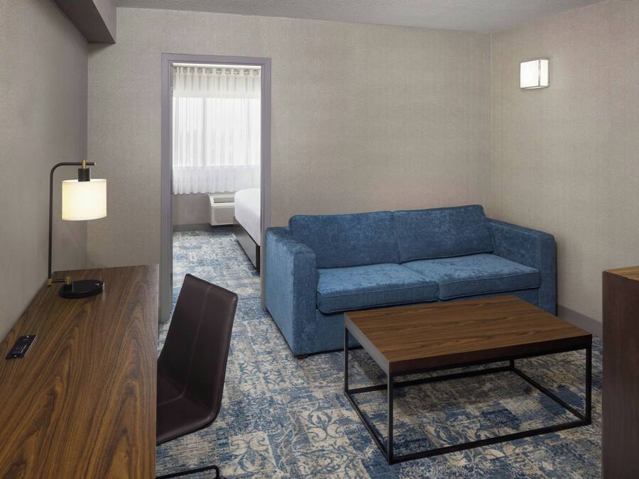 Habitación de hotel con un escritorio de madera, un sofá azul, una mesita de madera y una alfombra estampada.