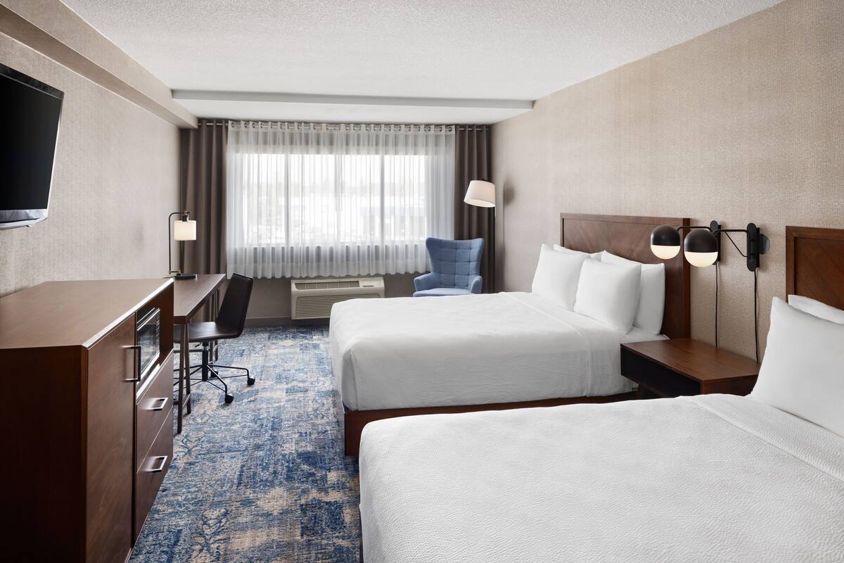 A hotel room with two beds, a desk, a chair, a TV, and a window with curtains.