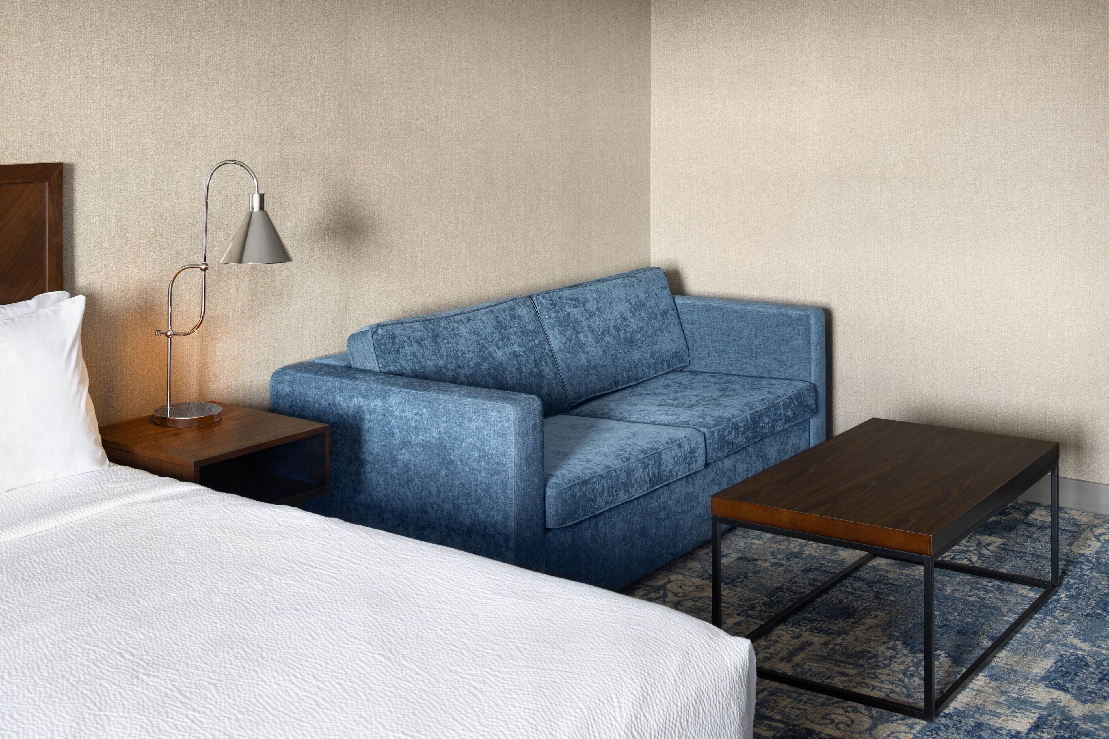 Ein Hotelzimmer mit einem Bett, einem blauen Sofa, einem kleinen Holztisch und einer Stehlampe.