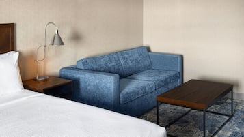 Ein Hotelzimmer mit einem Bett, einem blauen Sofa, einem kleinen Holztisch und einer Stehlampe.