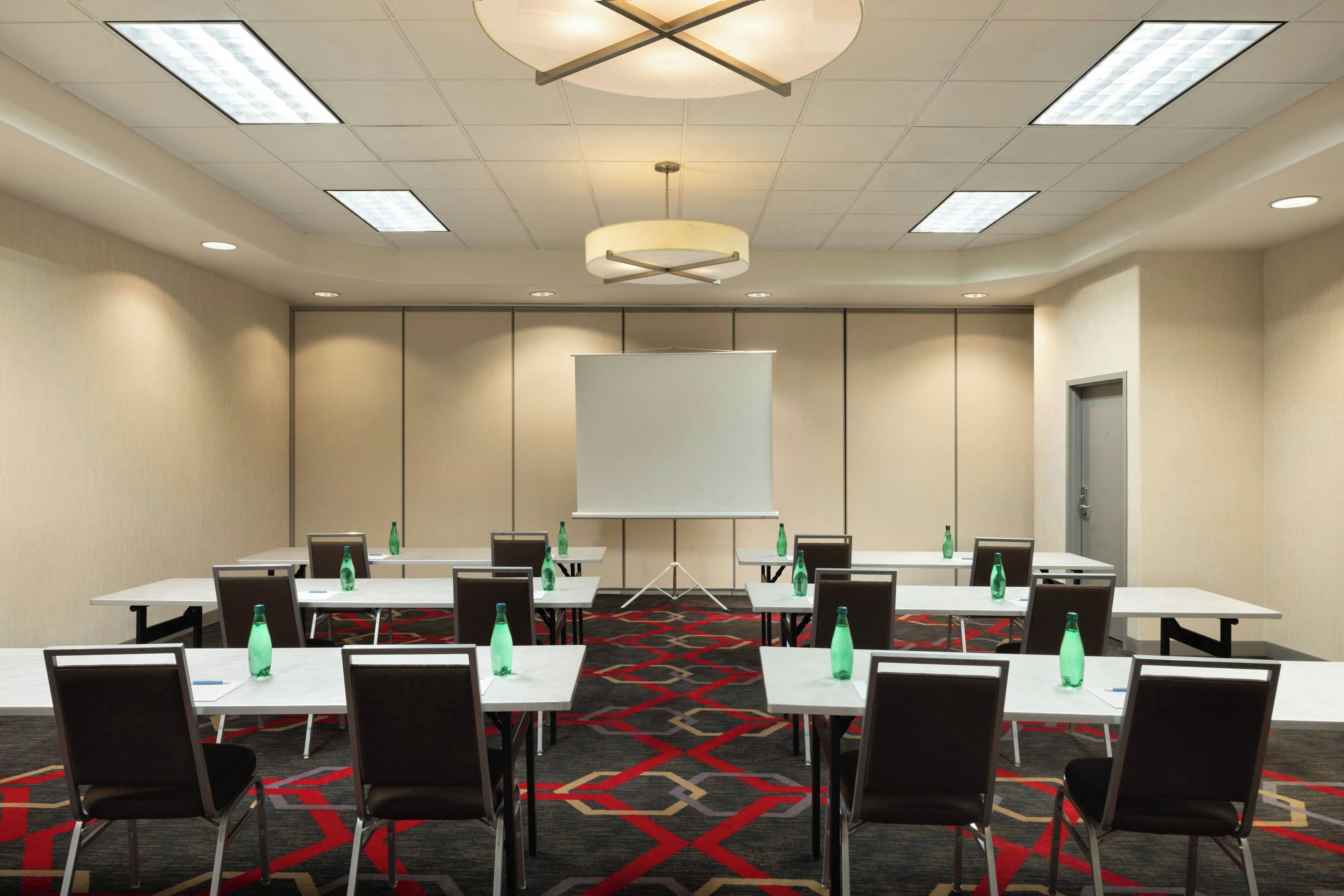 Ein Konferenzraum mit einer großen Whiteboard-Tafel, mehreren Tischen, Stühlen und Wasserflaschen.