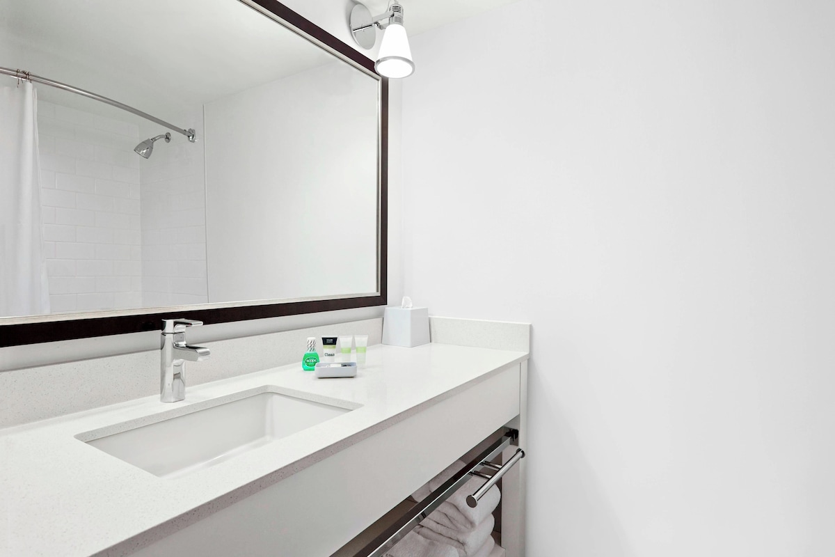 Un baño moderno con un lavamanos blanco, un espejo, un perchero para toallas y una cortina de ducha.