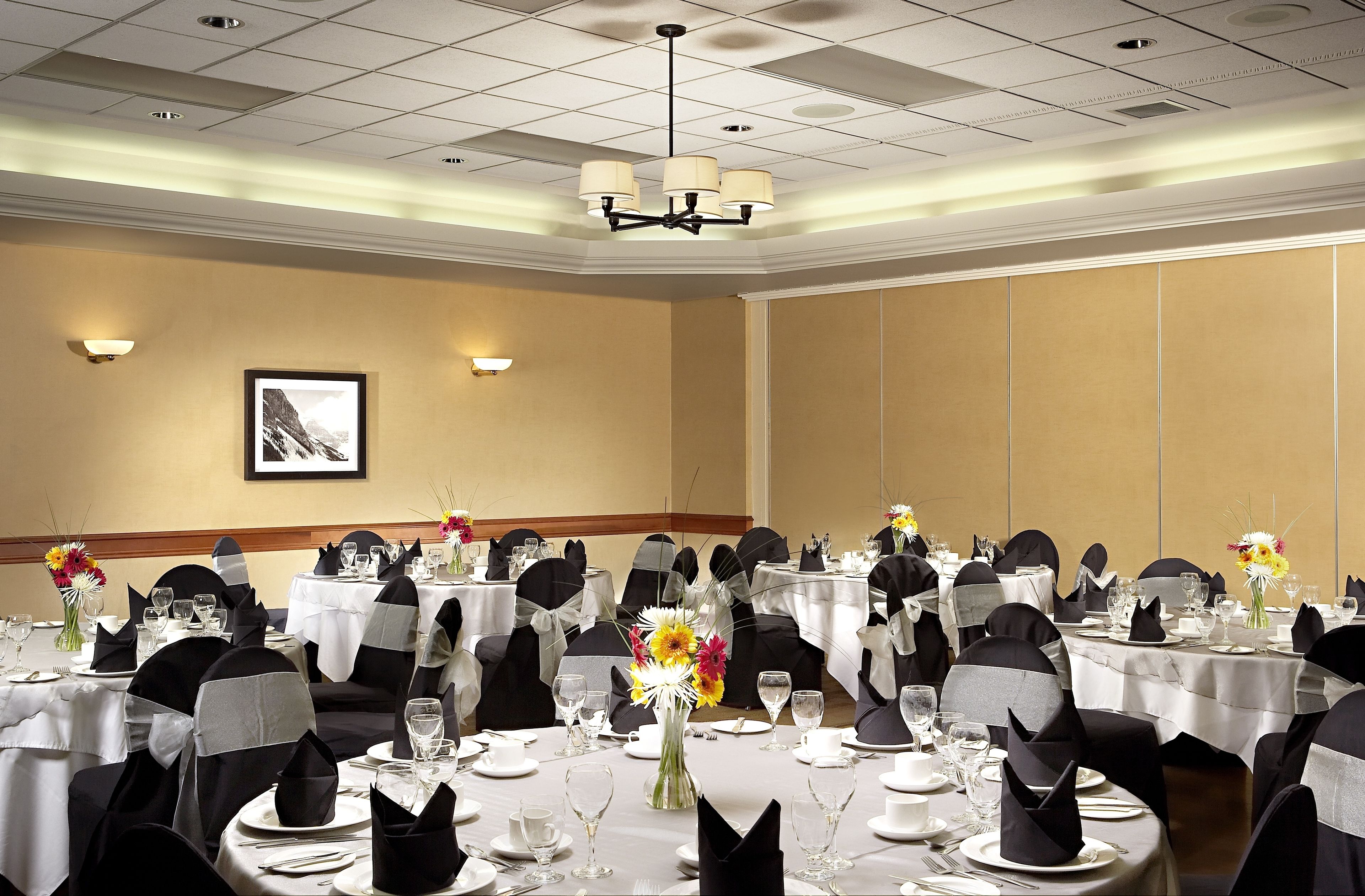 A banquet hall with multiple round tables set for dining, featuring black and white tablecloths, black chair covers, and floral centerpieces.