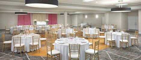 A large conference room with multiple round tables, each set with white tablecloths and gold chairs, arranged on a patterned carpet.