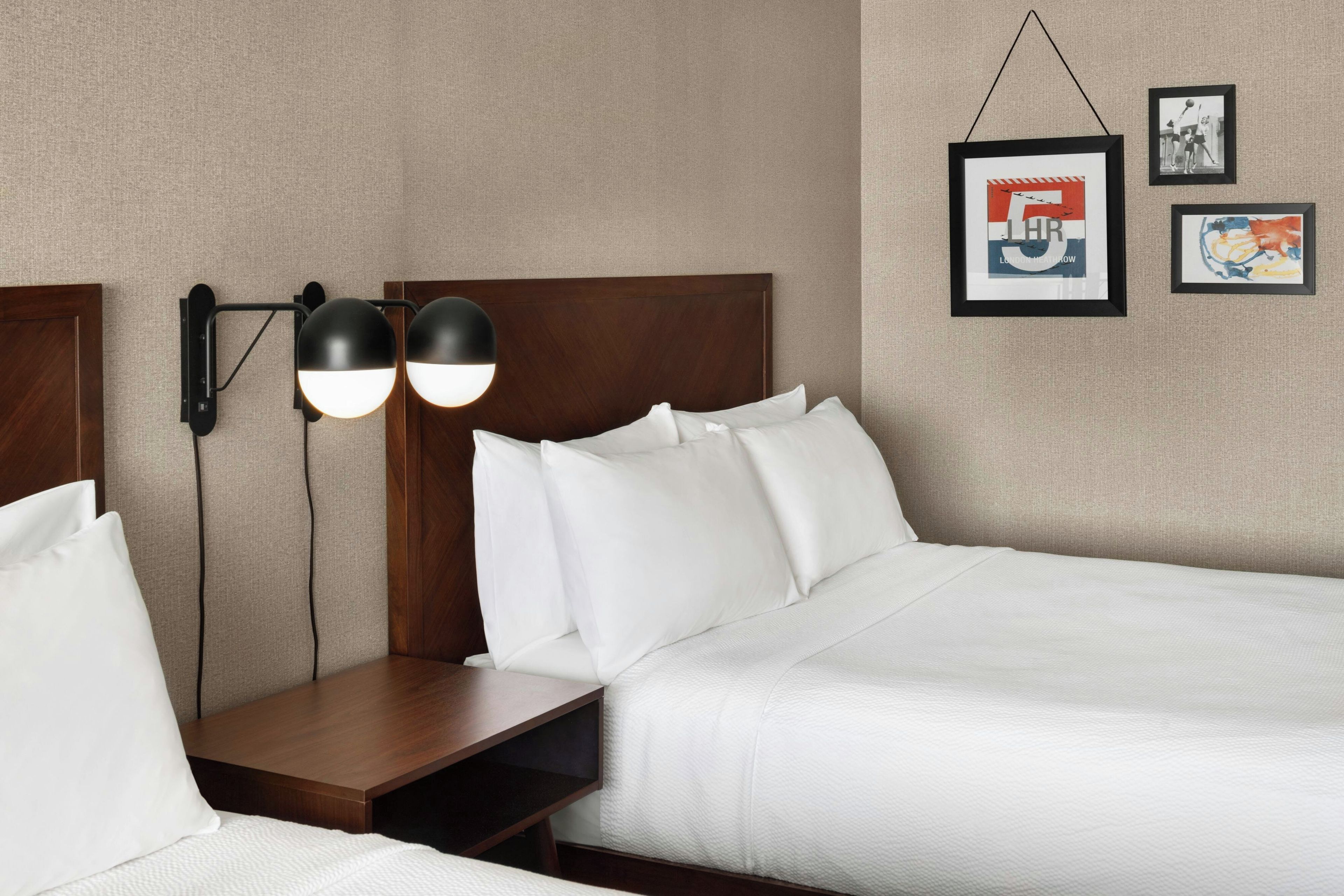 Habitación de hotel con cabecera de madera, dos mesitas de noche, cama con ropa de cama blanca y lámparas fijadas a la pared.