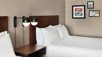 Habitación de hotel con cabecera de madera, dos mesitas de noche, cama con ropa de cama blanca y lámparas fijadas a la pared.