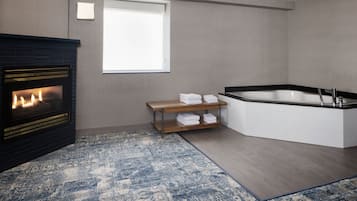 A modern bathroom with a bathtub, a fireplace, and a wooden shelf with towels.