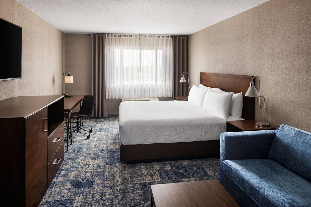 A hotel room with a large bed, a desk, a chair, a sofa, and a TV.
