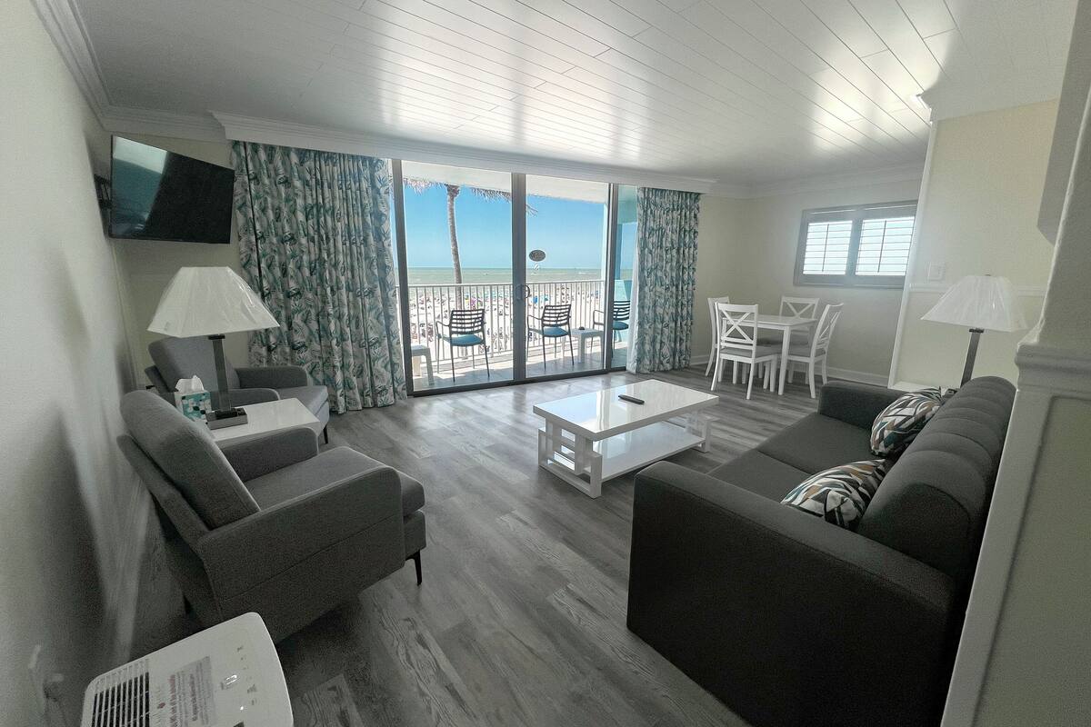 A modern living room with a balcony, grey sofas, a coffee table, and a flat-screen TV.