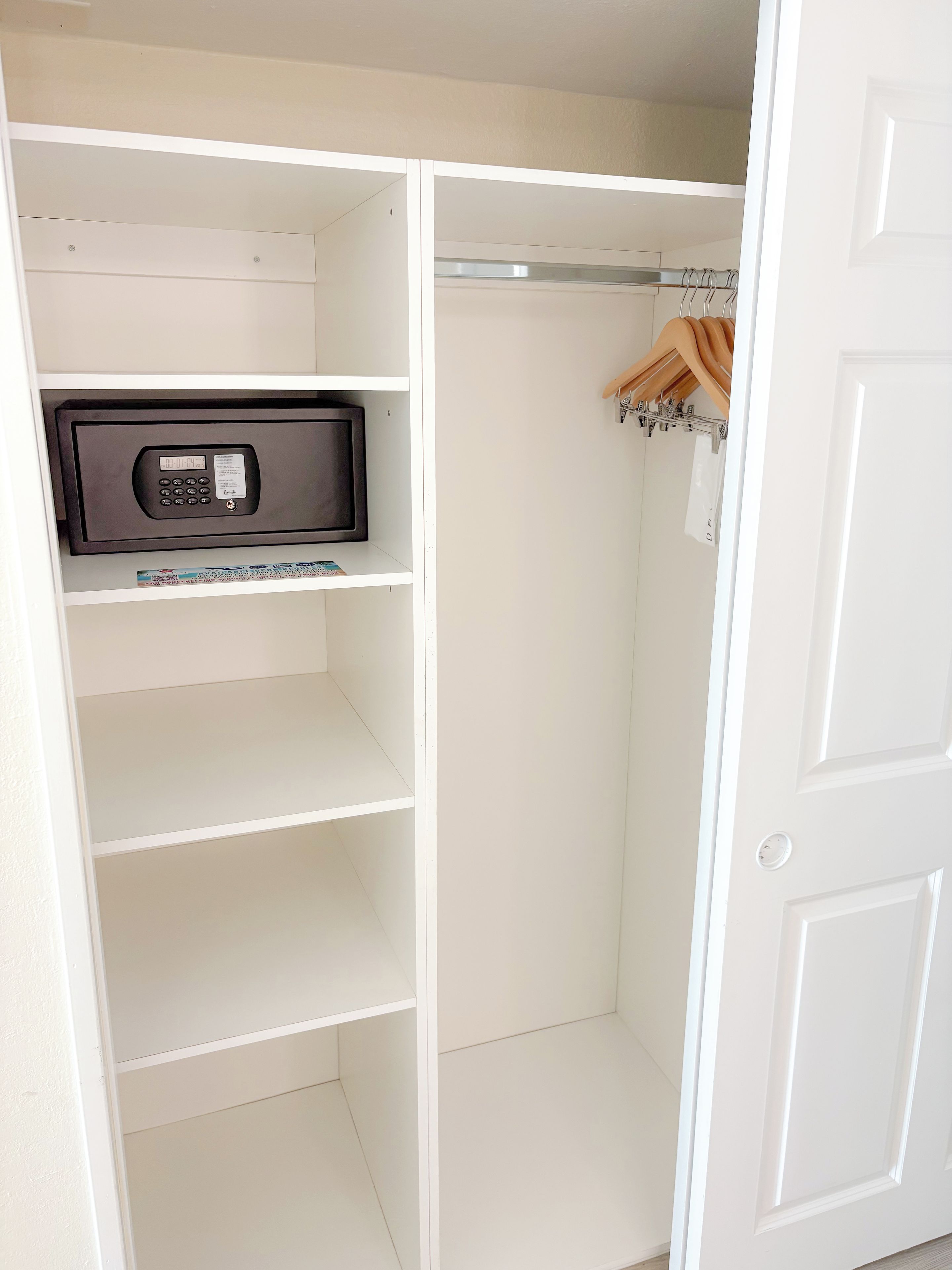 Un placard blanc avec des étagères, une tringle pour suspendre les vêtements et un four à micro-ondes placé sur l’étagère supérieure.