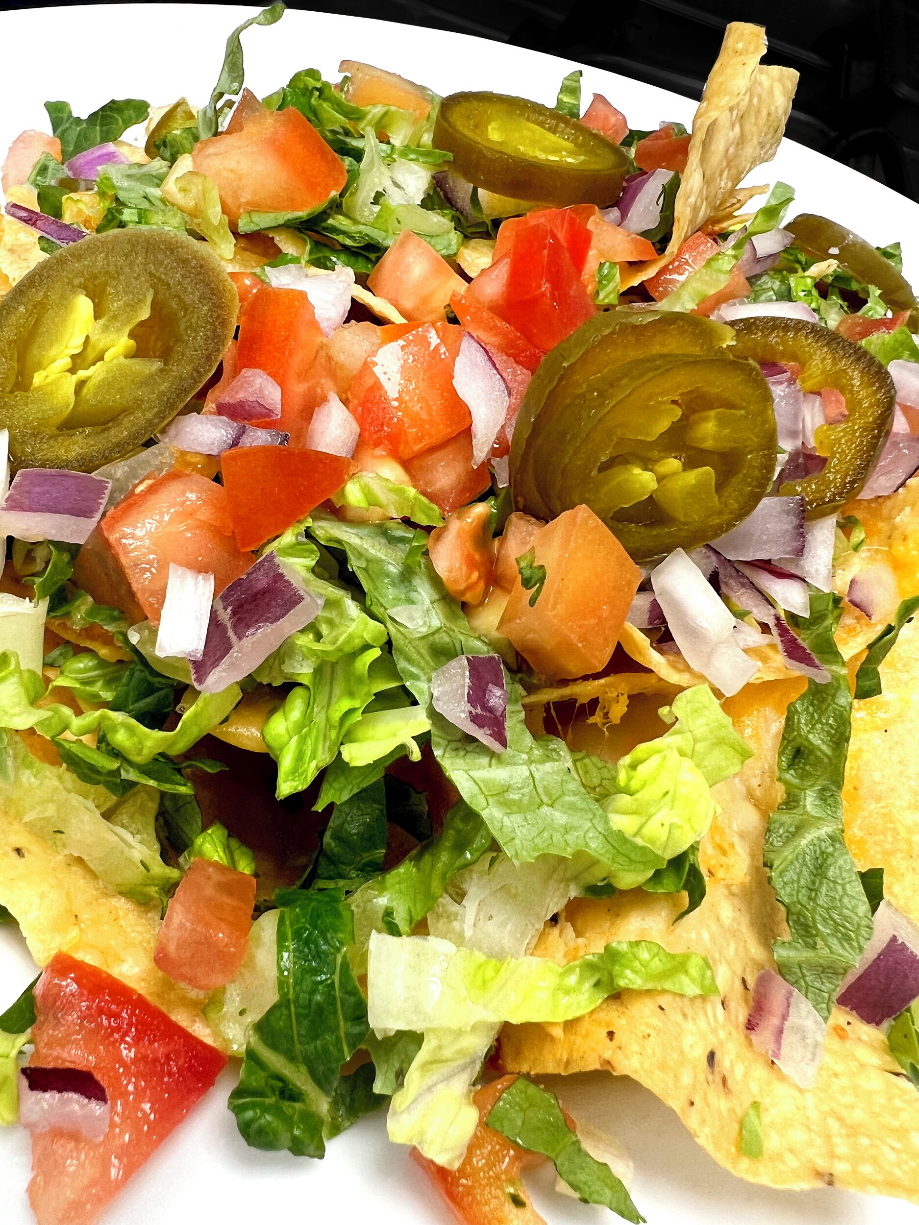 A plate of nachos topped with lettuce, tomatoes, onions, and jalapeños.