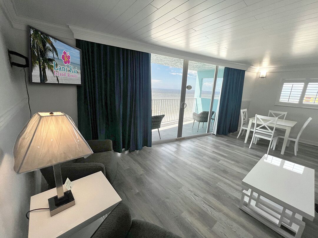 Une chambre d’hôtel avec un balcon, une table, des chaises, une lampe et un panneau indiquant qu’il s’agit d’un complexe hôtelier.