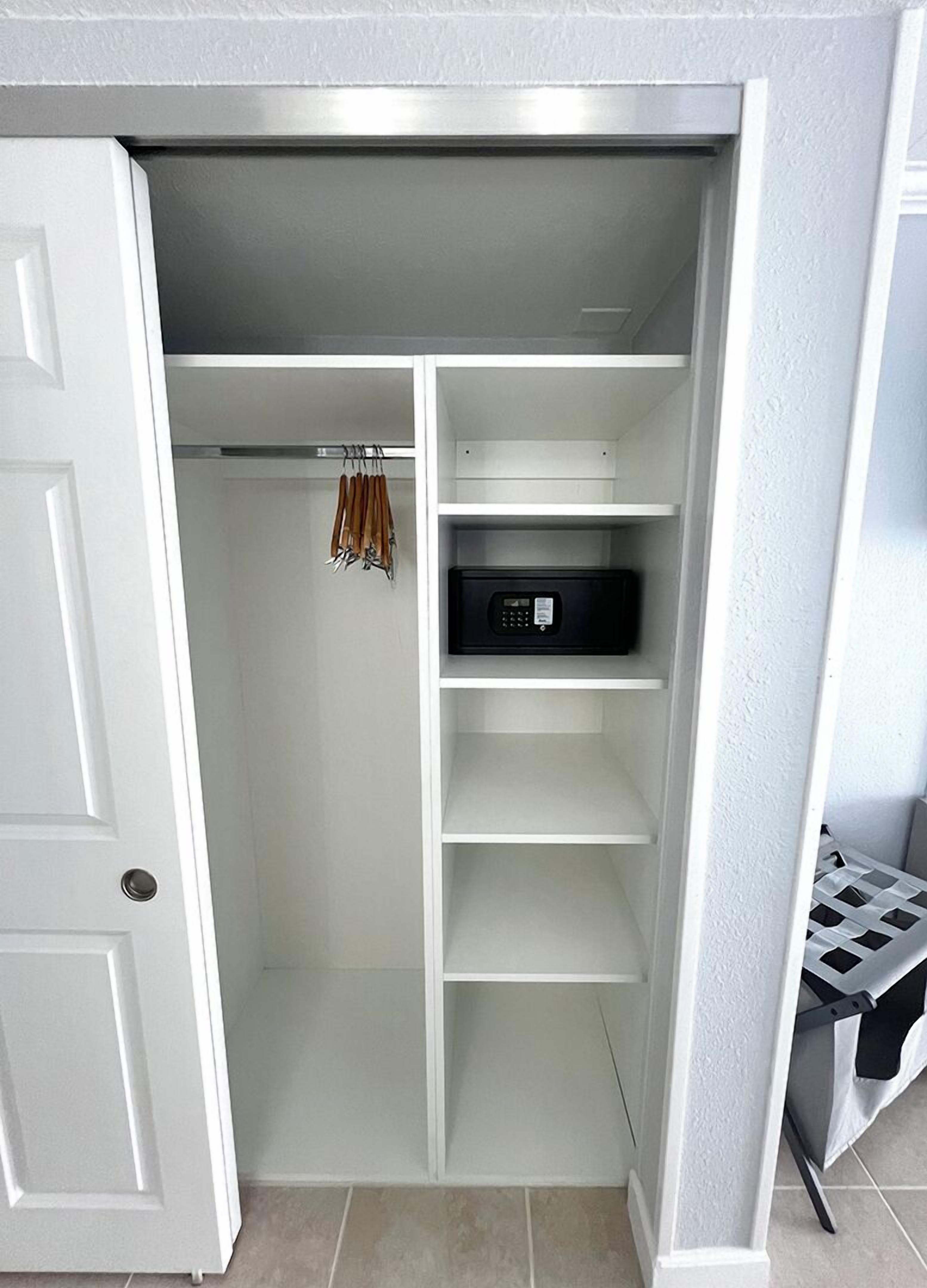 Un vestidor con estanterías blancas, un electrodoméstico negro y una barra para colgar ropa.
