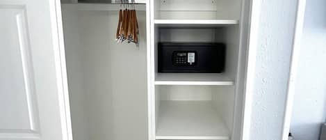 Un vestidor con estanterías blancas, un electrodoméstico negro y una barra para colgar ropa.