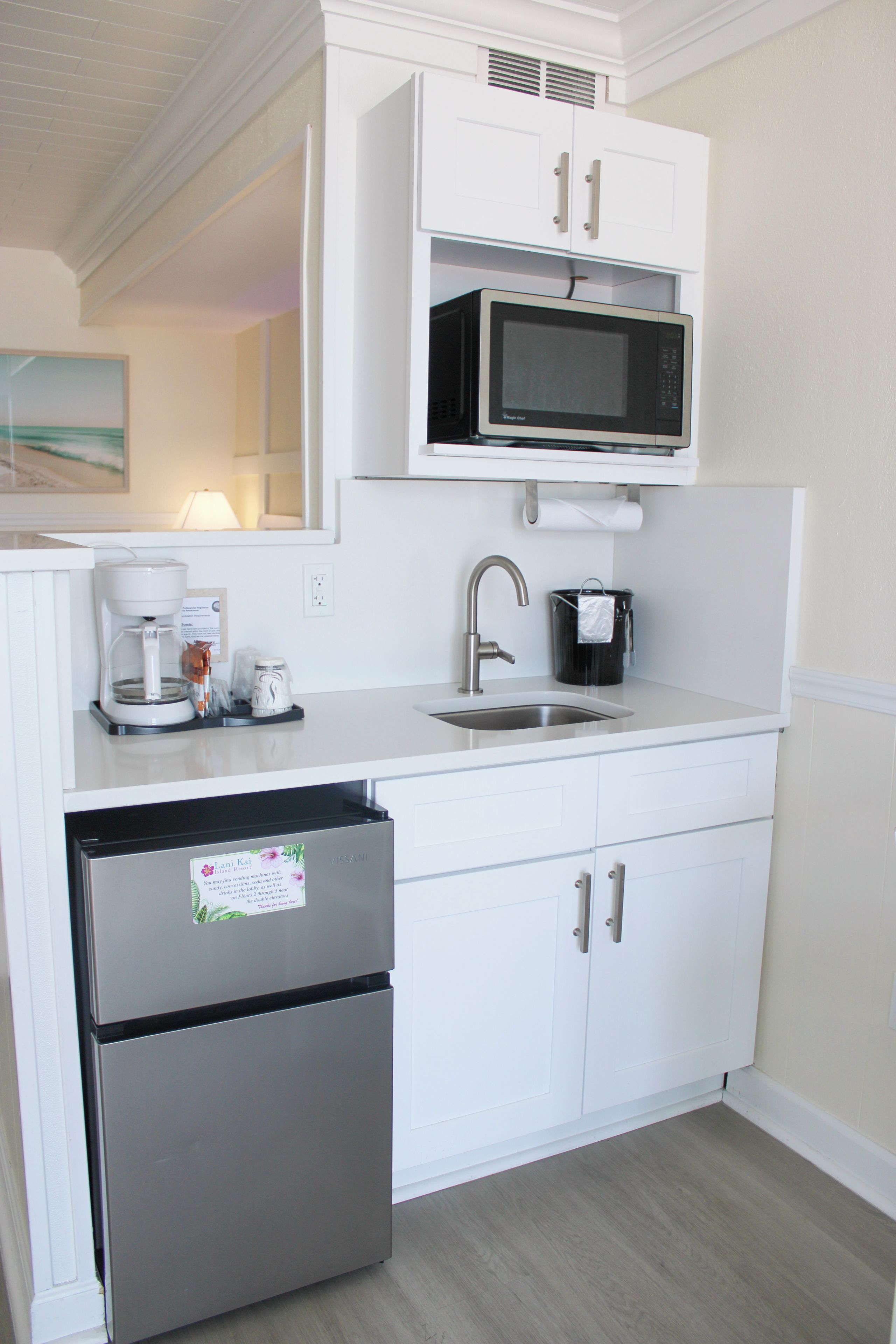 A compact kitchenette with a stainless steel refrigerator, a microwave, a coffee maker, and a sink.