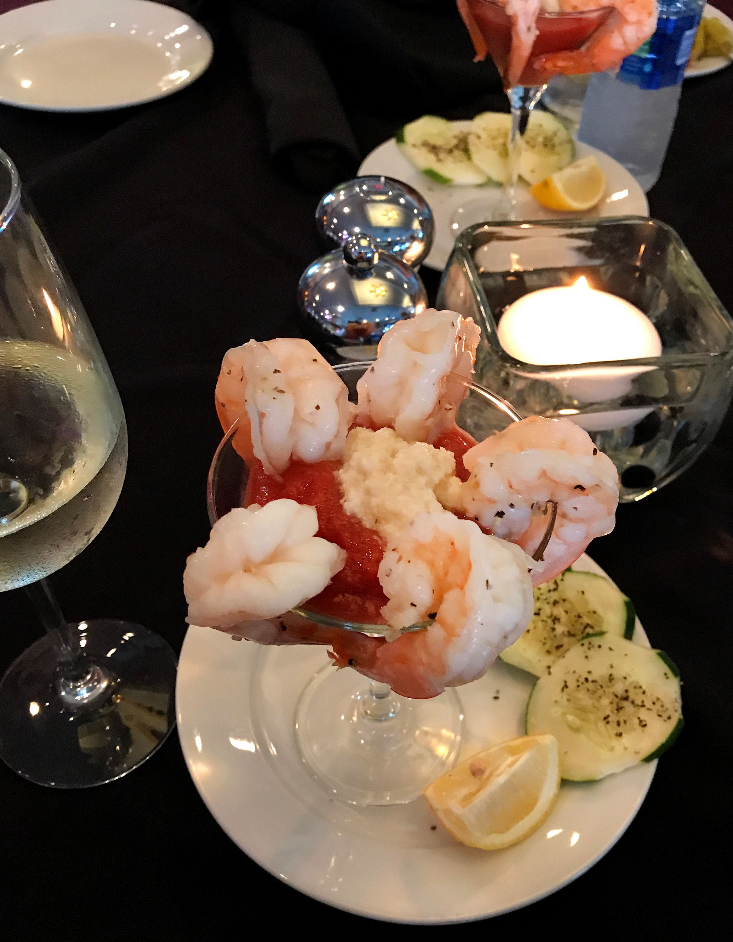 Ein Fischgericht mit Garnelen und Zitrone auf einem Teller, dazu ein Glas Weißwein und eine Kerze.