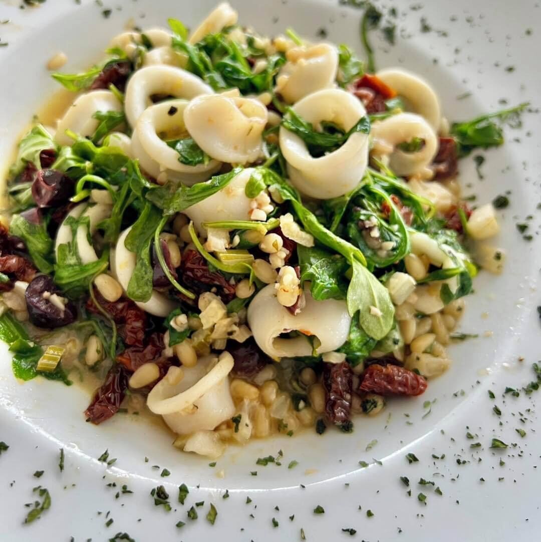 A plate of pasta with greens, nuts, and sun-dried tomatoes.