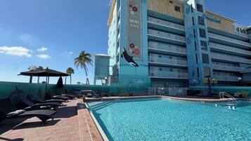 Zona de piscina con sillones de descanso y un mural en el edificio.