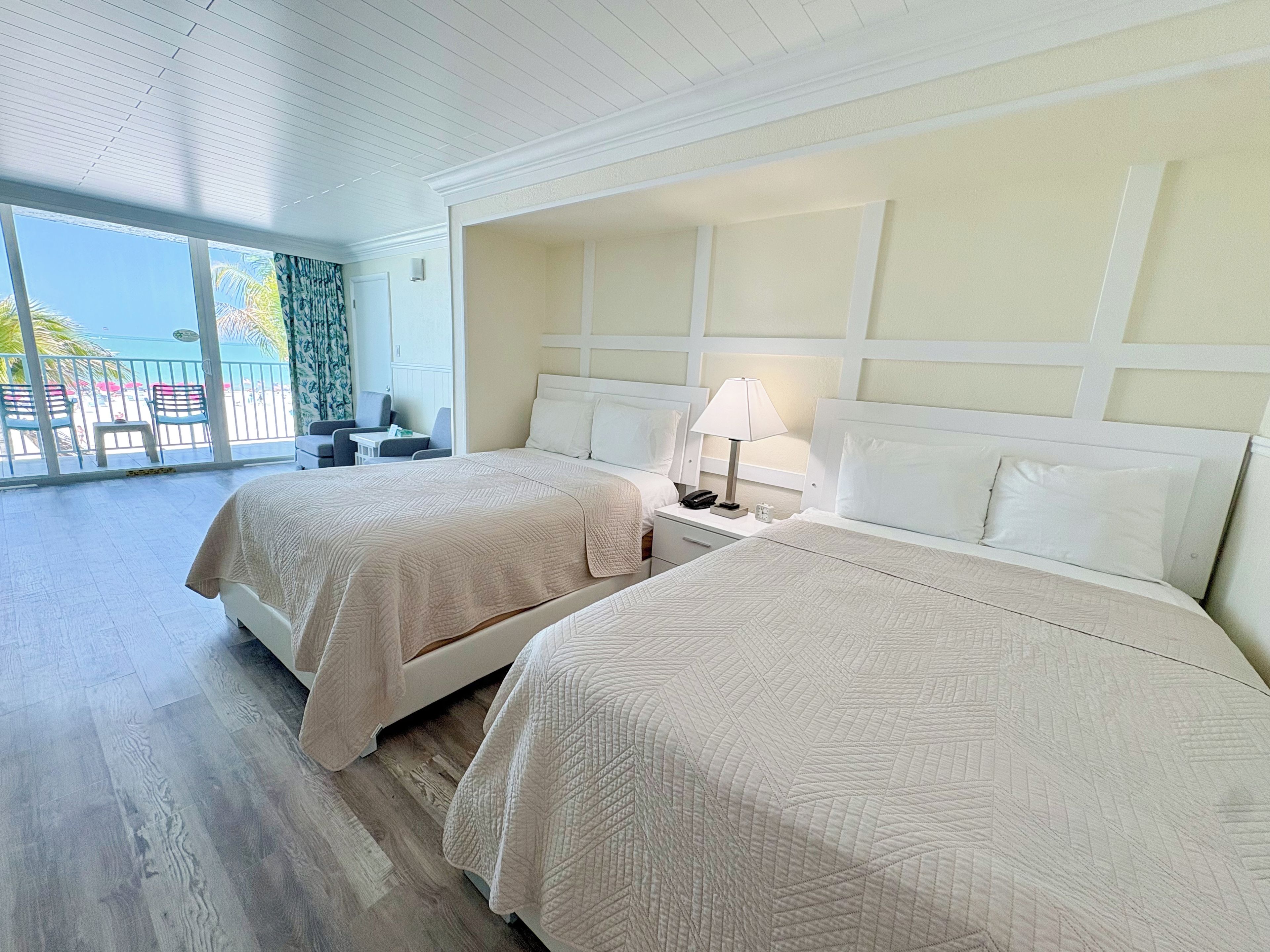 A hotel room with two beds, a balcony with a view, and a small table with a lamp.
