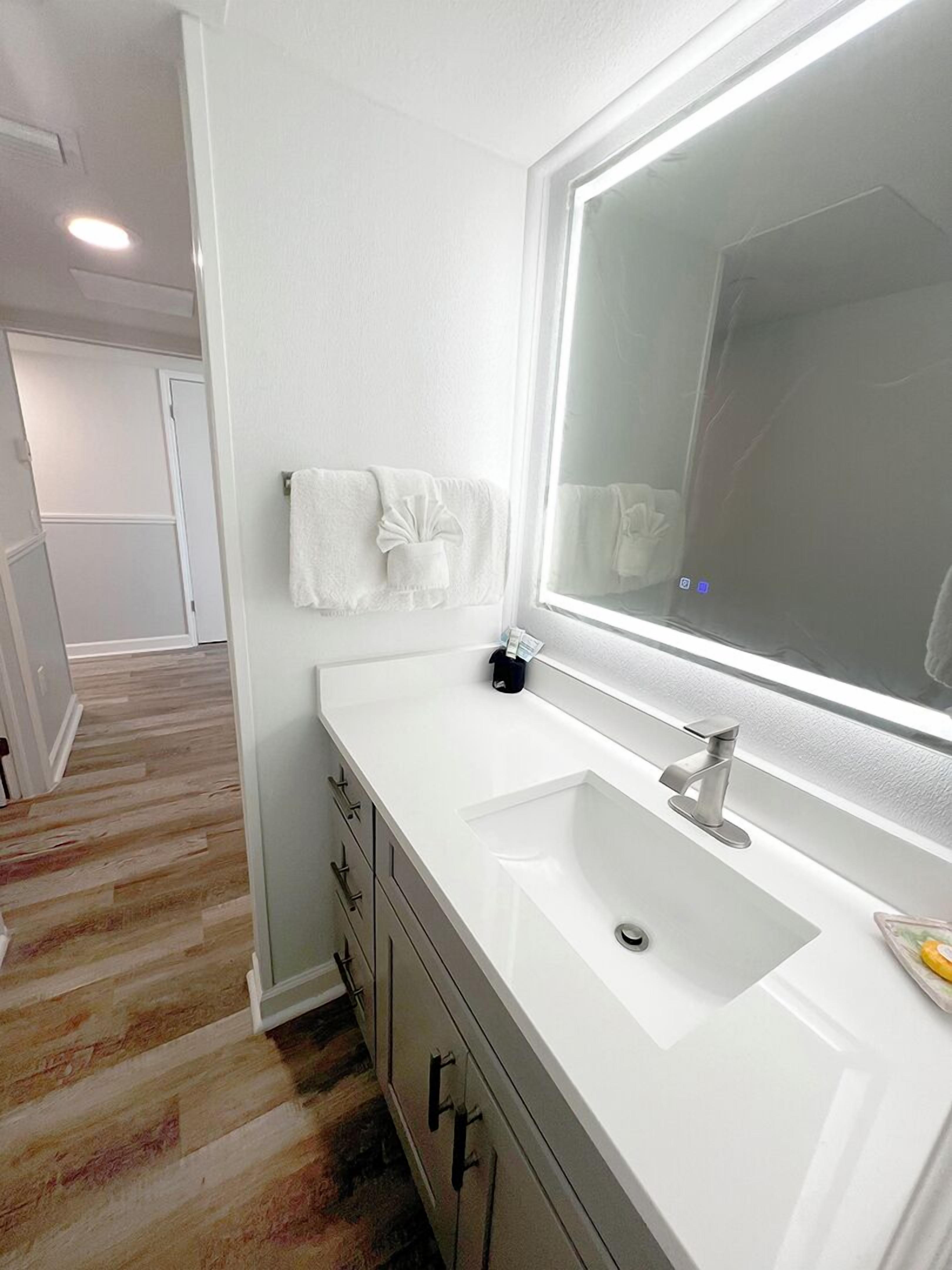A modern bathroom with a white sink, a large mirror, and a towel rack.