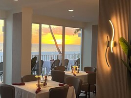 A restaurant with tables and chairs, a view of the ocean, and a sunset.